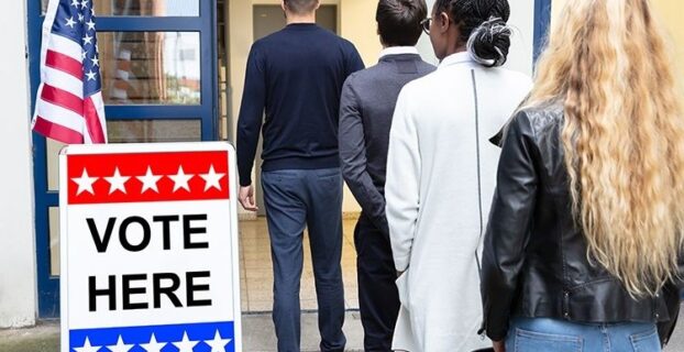 Voters enter a polling place beside a sign reading “VOTE HERE”