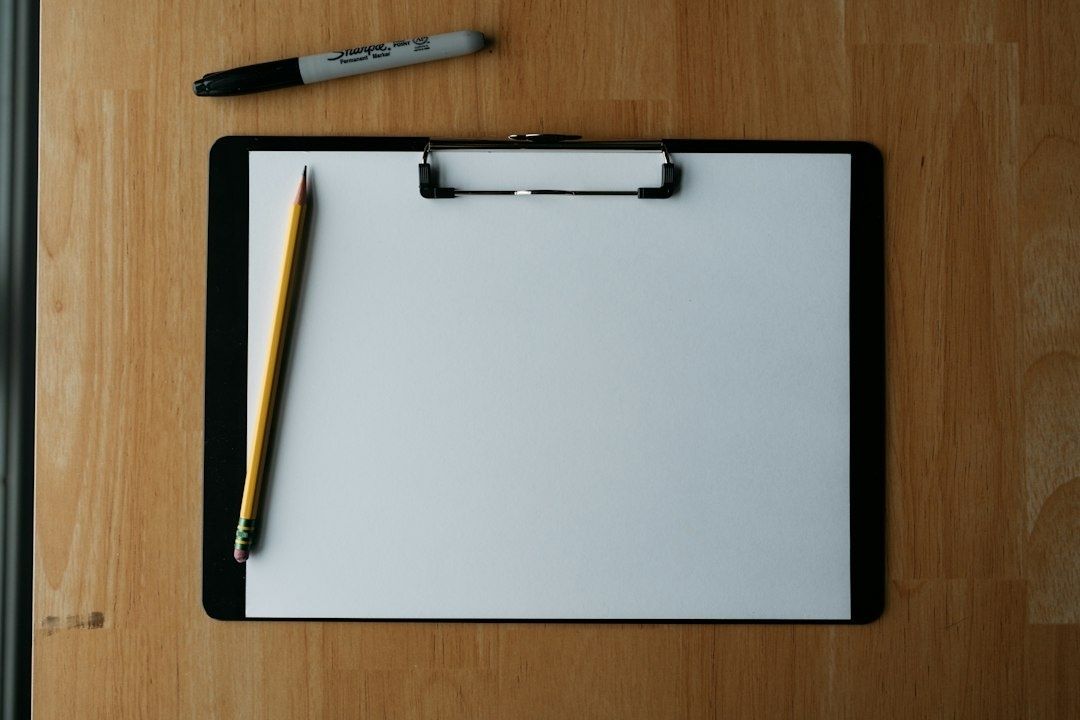 Blank clipboard and pencil beside a marker on a wooden desk